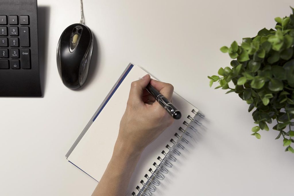 Woman's hands with pen writing on notebook. Modern grey office desk. Working, writing concept